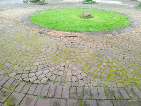 Circular paved stone pathway with green grass and flowers Stock Photos