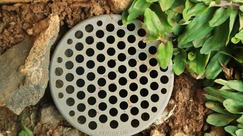 Circular plastic drain cover efficiently channeling water, set amid loose s.. Stock Photos