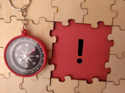 A circular red and black magnetic compass lies on a wooden jigsaw puzzle ne.. Stock Photos
