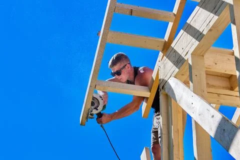 Circular saw cuts timber board as young construction worker trims wooden ro.. Stock Photos