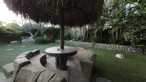 Circular stone bench under a thatched umbrella in a backyard garden Stock Footage 345543958