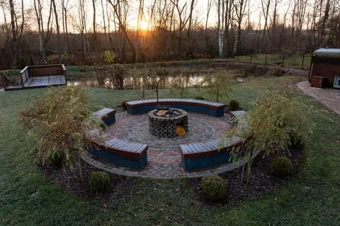 Circular stone fire pit on patterned patio with curved benches at dusk 스톡 사진