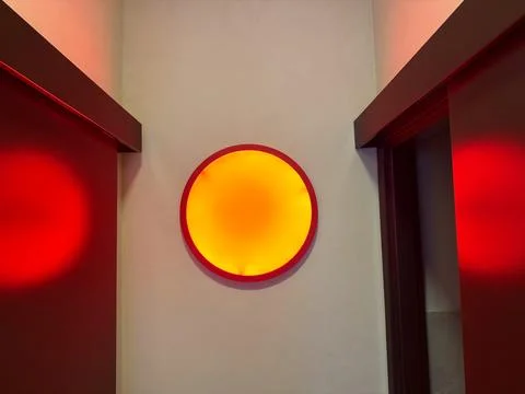Circular wall light glowing in red and yellow tones against neutral wall. Geo Stock Photos