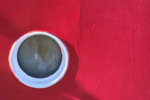 Circular window of a ship on bright red hull surface Stock Photos