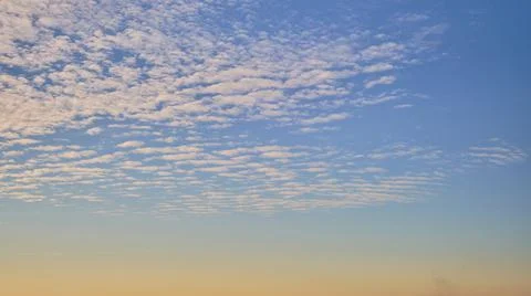 Cirrocumulus clouds in the evening at orange sunset, time-lapse against blue  Stock Photos