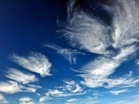 Cirrus clouds stretch across a bright blue sky in a vast scene of nature at.. Stockfoto's