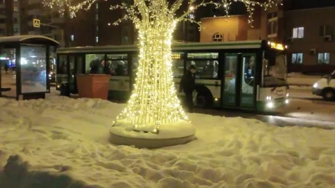 City bus stop next to a tree decorated with garlands and a departing bus 库存影片 147328277