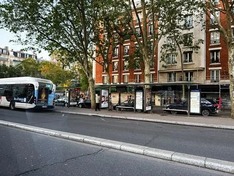 City bus stop on a tree lined street in Paris, France with commuters waitin.. Stock Photos