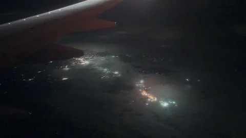 City lights glowing through clouds below airplane wing at night Video stock 347984143