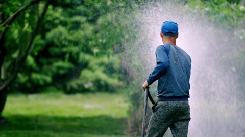 City worker in regular clothing waters lawn in city park Stock Footage 246054432