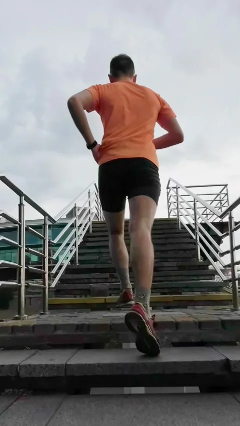 Cityscape Jog: Camera Trailing Runner in Orange Tee Climbing Stairs. Vertic.. Stock Footage 246669667