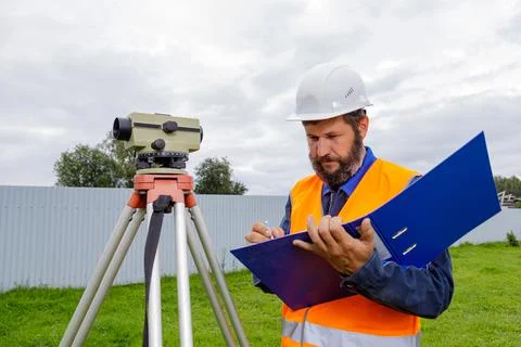 A civil engineer writes down the readings of the optical level on a piece of Stock Photos