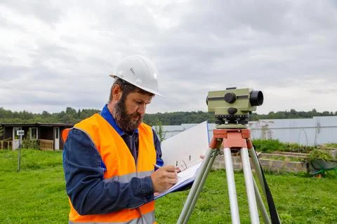 A civil engineer writes down the readings of the optical level on a piece of Stock Photos
