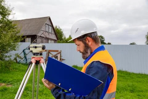 A civil engineer writes down the readings of the optical level on a piece of  Stock Photos