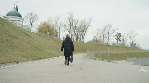 Clad figure strolling. Someone dressed in black coat walking purposefully along Stock Footage 334958799