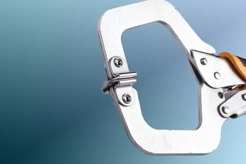 A clamp is placed on a white surface. It features a metal frame with orange r Stock Photos