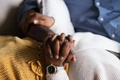 Clasped hands are resting on sofa with wristwatch, mustard knit throw, cream Stock Photos