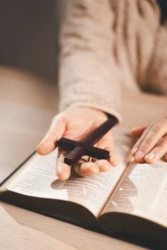 Clasped hands in prayer over an open book, warm light and shallow depth of .. Stock Photos