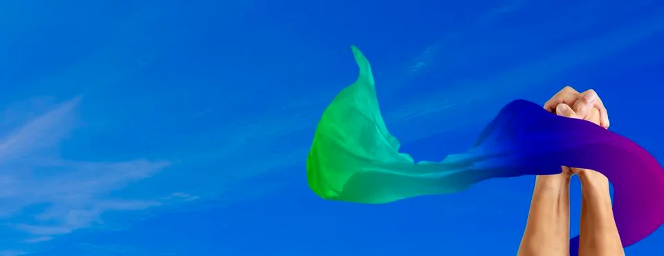 Clasped hands of two men surrounded with rainbow fabric flag with blue sky ba Stock Photos
