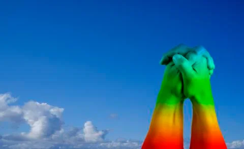 Clasped hands of two menpainted as the rainbow flag with blue sky background. Stock Photos