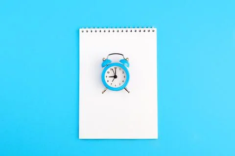 Classic alarm clock and empty notepad on blue background. Stock Photos
