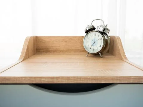 Classic analog clock with silver tick bell on nightstand or wooden bedside table Stock Photos