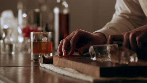 Classic bartender cutting a thin slice of an orange peel for garnish in interior Video stock 199456101