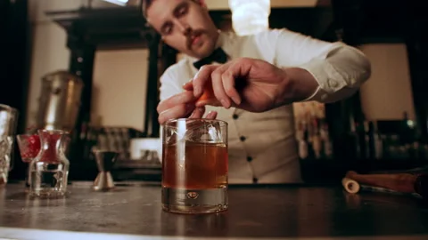 Bartender peels orange peel for cocktail at bar Stock Photo by