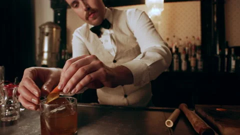 Classic bartender garnishing an old fashioned cocktail with an orange peel and c Stock Footage 199463219