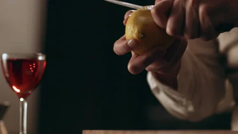 Classic bartender peeling a lemon peel with a knife for garnish in interior clas Stock Footage 199460048