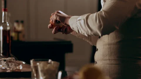 Classic bartender peeling an orange with a knife in interior classy bar with sof Stock Footage 199457012