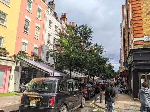 A classic black cab drives down a vibrant street with colourful buildings in Stock Photos
