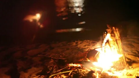 Classic campfire burning brightly with snapping flames by riverside at night 库存影片 79954491