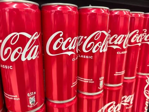 Classic Coca-Cola cans lined up on a supermarket shelf in vibrant red Stock Photos