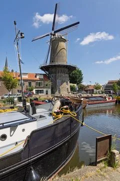 A classic Dutch windmill "De Roode Leeuw" in Gouda stands tall by a tranquil  스톡 사진