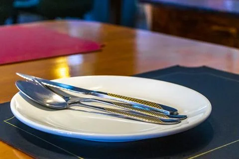 Classic elegant dining setup with empty plate and silverware on table. Stock Photos