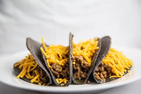 Classic hard shell blue corn tacos with ground beef and cheese on white plate Stock Photos