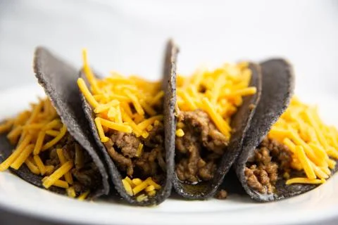 Classic hard shell blue corn tacos with ground beef and cheese on white plate Stock Photos