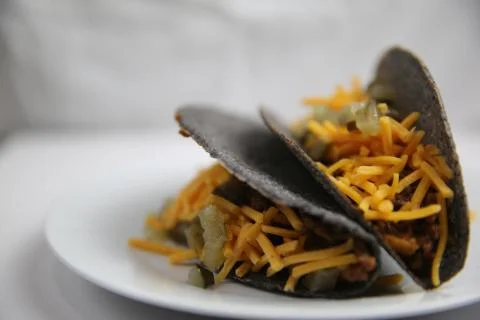 Classic hard shell blue corn tacos with ground beef and cheese on white plate Stock Photos