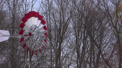 Classic Metal Farm Windmill with Red and White Blades Against Winter Trees Stock Footage 335598144