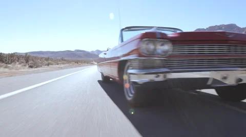Classic red Cadillac convertible cruising down sunny desert highway. Stock Footage