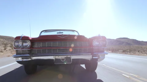 Classic red Cadillac convertible as it drives down a sunny desert road. Stock Footage