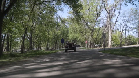 Classic red convertible car driving along a tree-lined road in a beautiful park Stock Footage 344169238