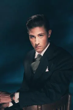 Classic stylish vintage man in suit and tie. Hair combed back. Dark blue back Stock Photos