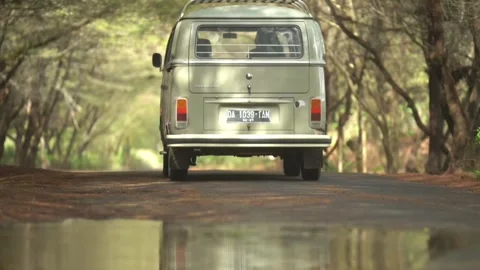 A classic van cruises down a quiet, tree-lined road. Stockbeeldmateriaal 310548849