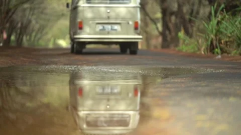 A classic van cruises down a quiet, tree-lined road. Stockbeeldmateriaal 310548850