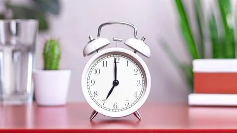 Classic white clock on a table. The clock hand points at 07:00, 19:00 close.. 스톡 사진