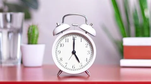 Classic white clock on a table. The clock hand points to 5 or 17, close up 스톡 사진