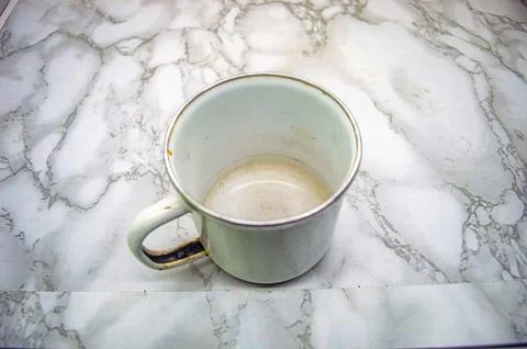 A classic white enamel mug with a silver rim, showing slight wear, rests on.. Stock-Fotos