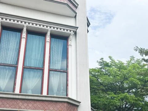 Classical White Building Facade with Elegant Red Window Frames and Green Foliage 库存照片